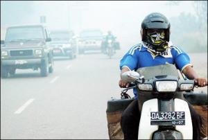 Afbeelding: Een motorrijder op Borneo trotseert de rook.